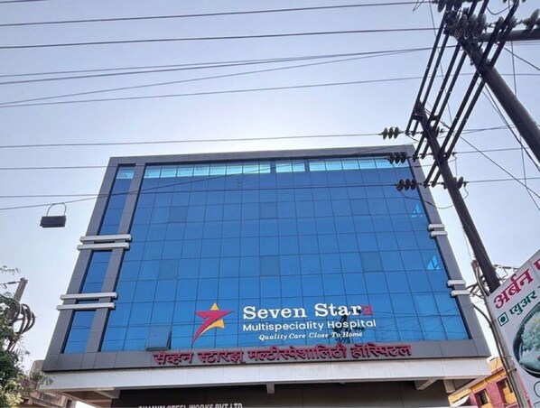 A modern building with a blue glass facade, featuring the logo and name 'Seven Star Multispeciality Hospital' and 'Quality Care Close To Home'.
