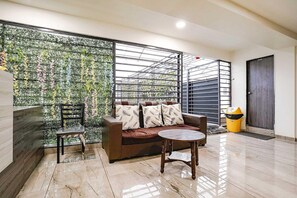 A modern living area with a sofa, a round table, and a chair. A decorative wall with plants is behind the sofa. - Hotel O Nashik Passport Office (Nashik)