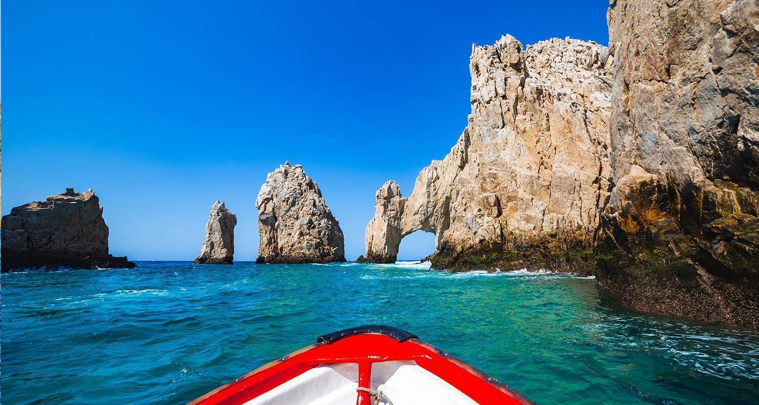 A boat in clear turquoise waters with rocky formations and a clear blue sky.