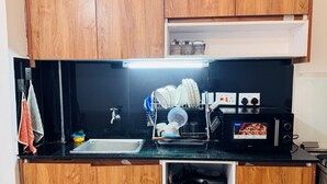 A compact kitchen with wooden cabinets, a black countertop, a microwave, and a sink. - 1Bedroom 1Bath | Perfect for Couples & Business (Nairobi)