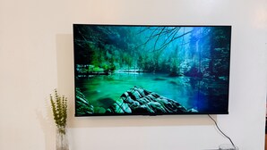 A flat-screen TV mounted on a wall with a black shelf below. - 1Bedroom 1Bath | Perfect for Couples & Business (Nairobi)