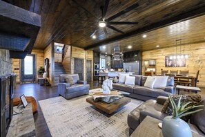 Amplia sala de estar con chimenea, sofás de cuero, una mesa de centro y una cocina al fondo.