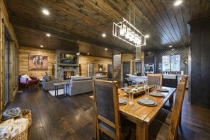 Amplia sala de estar con chimenea, una mesa de comedor para cuatro personas y una cocina al fondo.