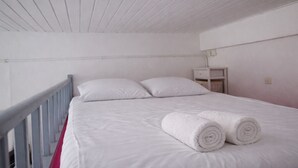 Ein weißes Bett mit zwei Kissen und zwei zusammengerollten Handtüchern, ein weißer Nachttisch und ein weißer Geländer.