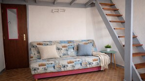 Ein Zimmer mit einer Couch, einem kleinen Tisch mit einer Pflanze und einer Holztreppe.