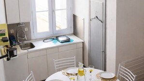 Eine kleine Küche mit Fenster, weißen Schränken und einer Essecke mit rundem Tisch für vier Personen.