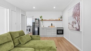 A compact living space with a green sofa, a kitchenette, and a dining area. - The Harla Beachside - ideally situated near the azure ocean, pristine beaches just a short stroll (Coffs Harbour)
