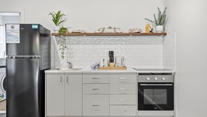 A kitchen with a stainless steel refrigerator, a built-in oven, and a countertop with a coffee maker and utensils. - The Harla Beachside - ideally situated near the azure ocean, pristine beaches just a short stroll (Coffs Harbour)