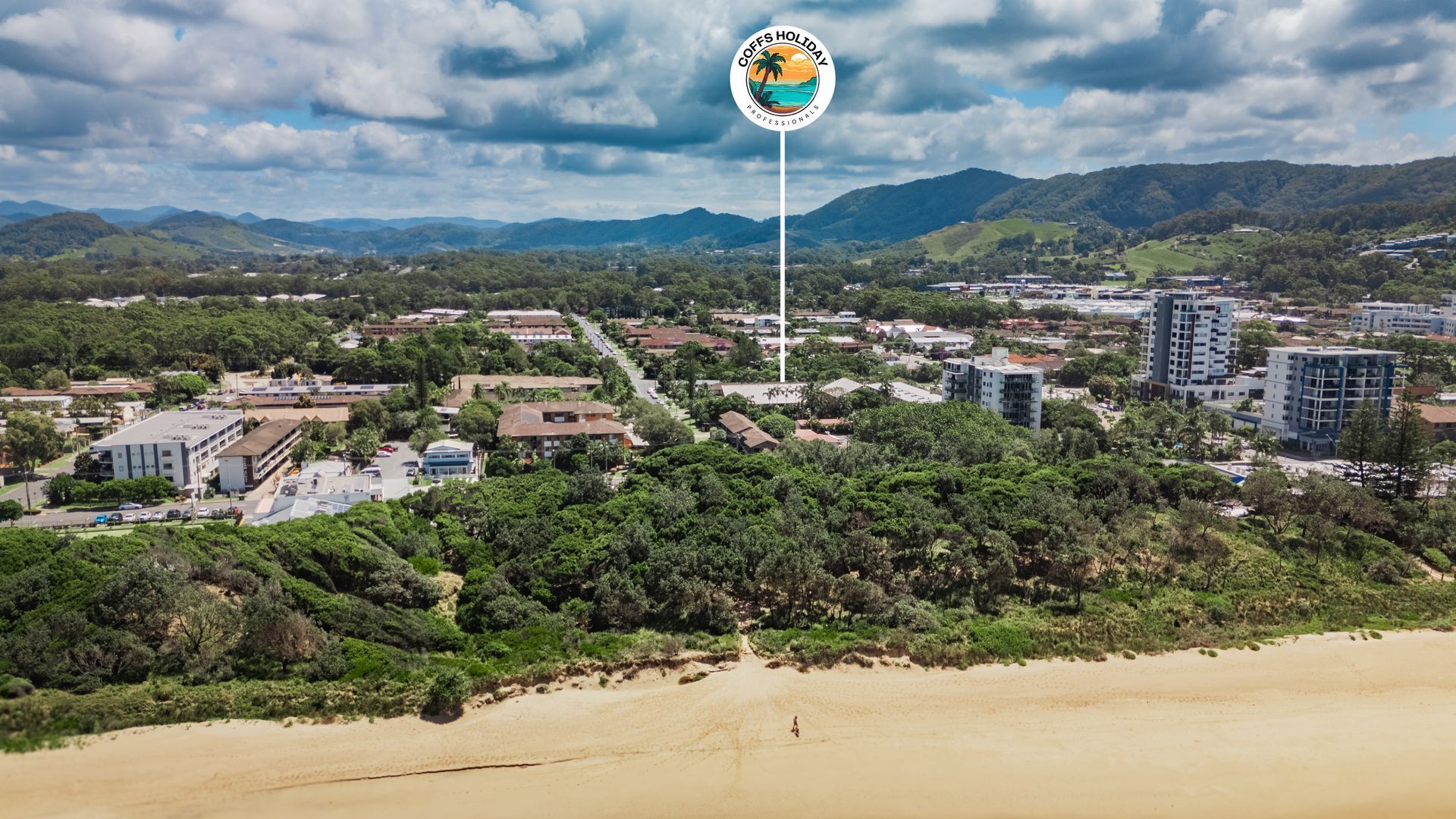 A coastal town with a mix of residential and commercial buildings, a sandy beach, and a logo for 'COFFS HOLIDAY PROFESSIONALS' on a flagpole.