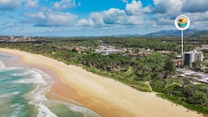 Blick auf die Küste mit Strand, Gebäuden und dem Logo von COFFS HOLIDAY PROFESSIONALS.