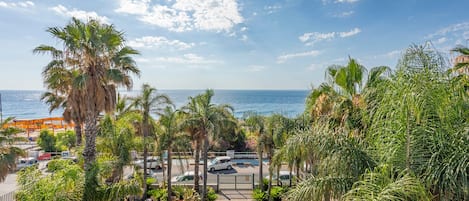 A view of a beachside area with palm trees, a pool, and a road leading to the sea.
