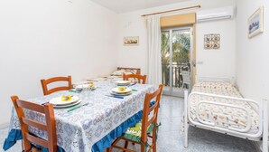 A room with a dining table set for four, a single bed, a balcony with a view, and a door leading outside. - Apartment 'I Ciottoli Dello Ionio - Apt 10' with Sea View, Shared Terrace and Balcony (Mascali)