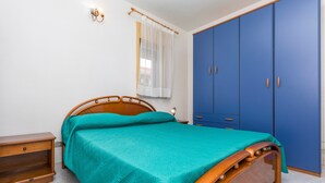 A bedroom with a bed, wooden nightstand, blue wardrobe, and a window with a white curtain. - Apartment 'I Ciottoli Dello Ionio - Apt 10' with Sea View, Shared Terrace and Balcony (Mascali)