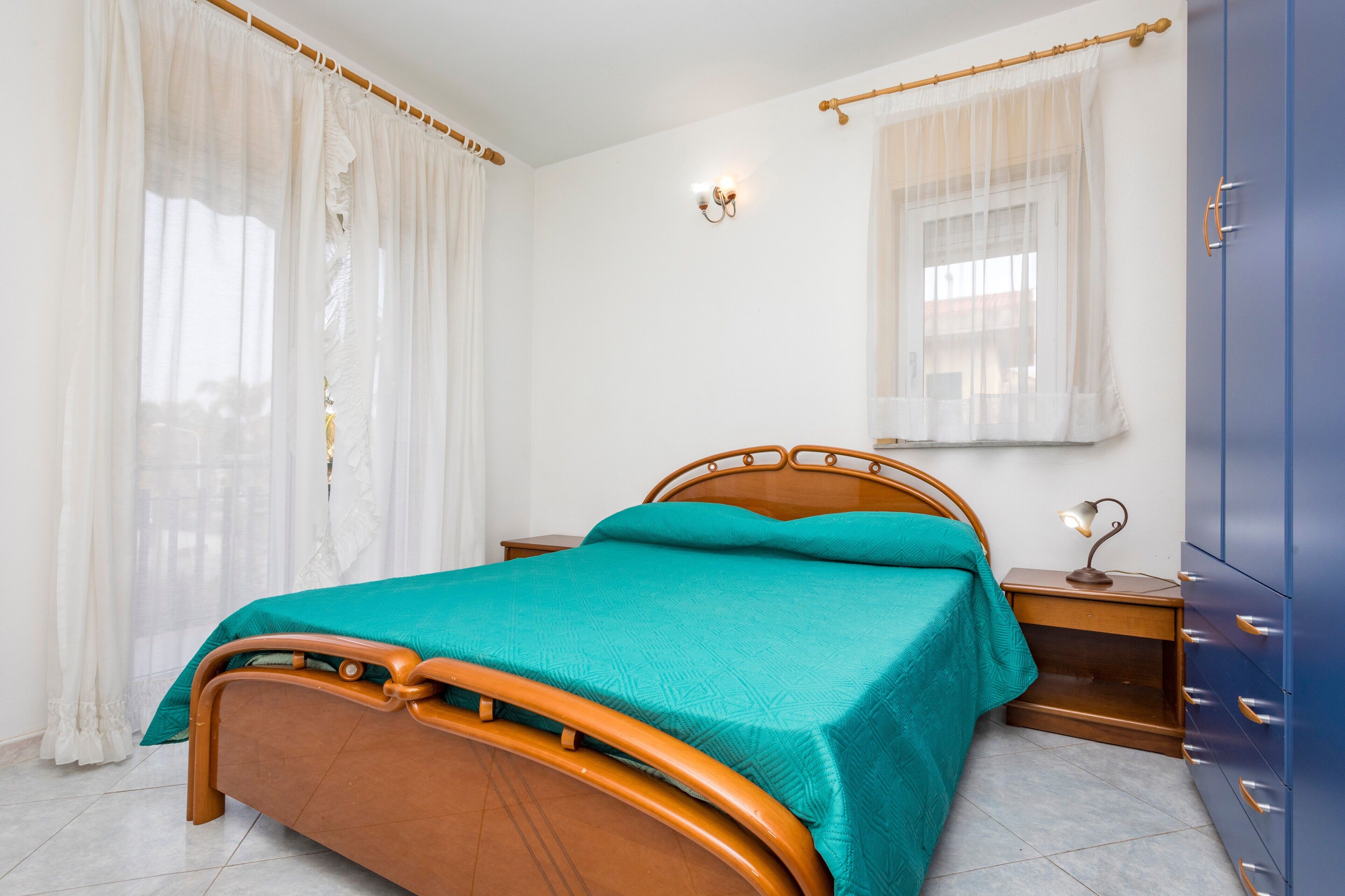 A bedroom with a bed, a nightstand, a lamp, a wardrobe, and a window with curtains.