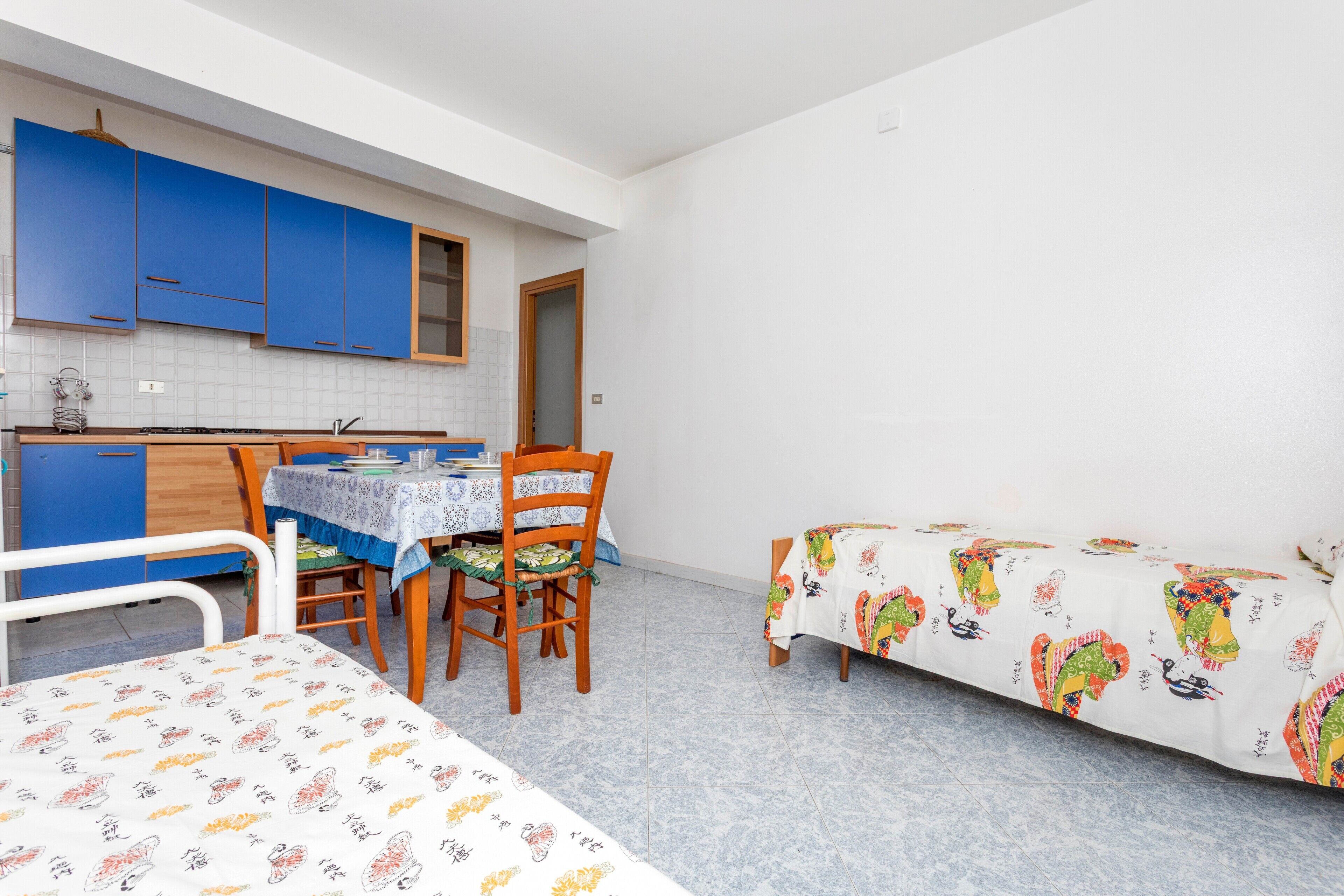 Una habitación compacta con cama, una mesa de comedor con sillas, kitchenette y un ventanal pequeño.