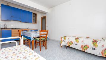 Habitació compacta amb llit, taula de dinar amb cadires, petita cuineta i finestra.