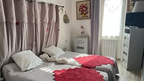 A bedroom with a bed, two pillows, a bedside table, a lamp, a dresser, and a window with curtains. - Bed and Breakfast 'Mas De Maussan' with Mountain View, Wi-Fi and Air Conditioning (Robion)
