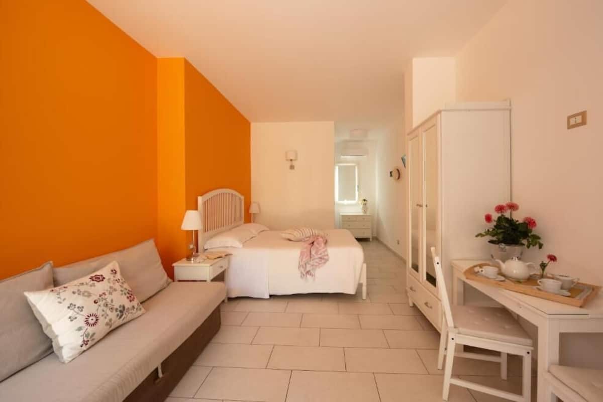 Quarto com cama, mesa de cabeceira, luminária, cadeira e escrivaninha com bandeja.