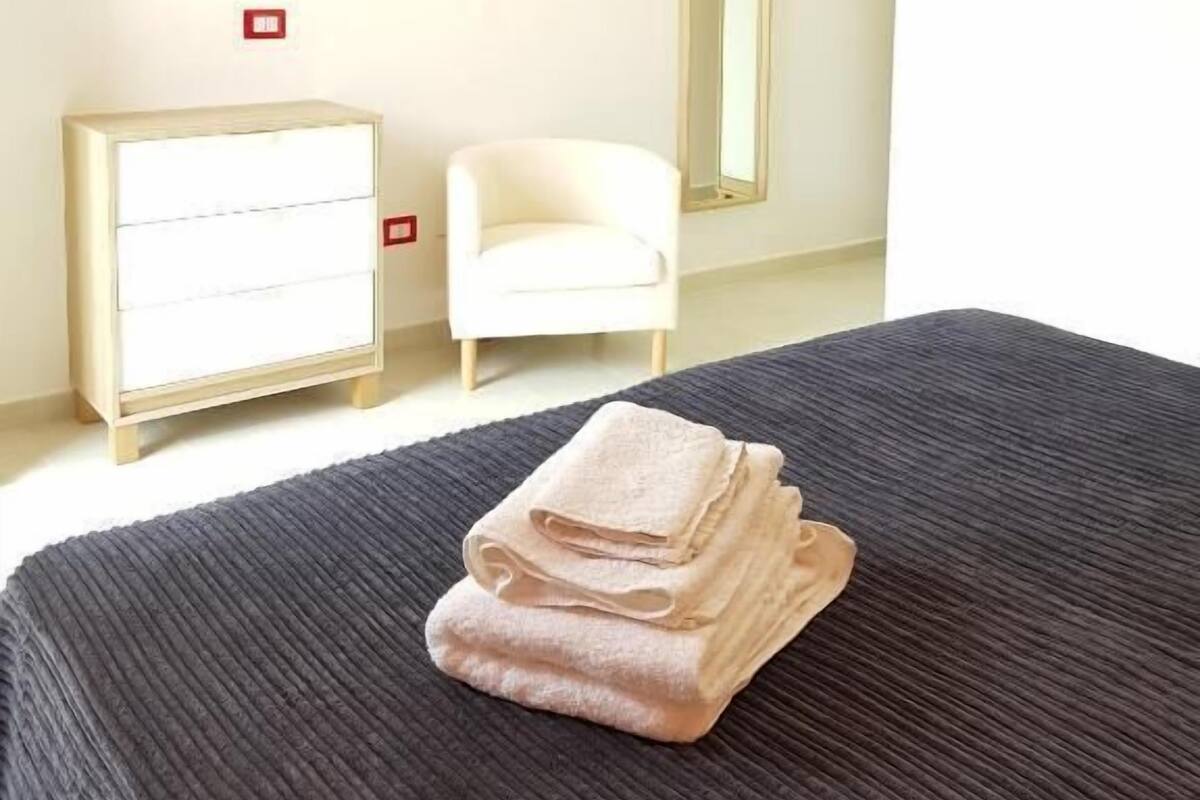 Quarto de hotel com cama, cômoda, cadeira, televisão e espelho.