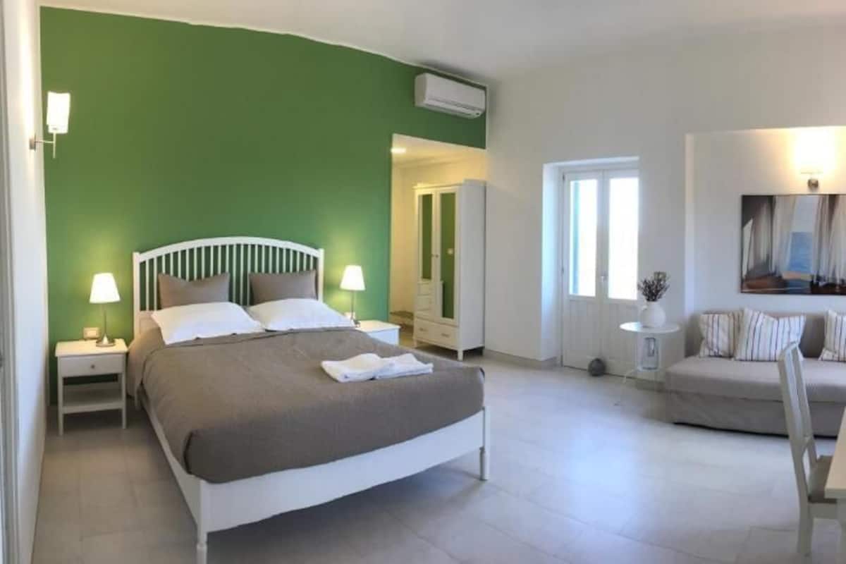 Quarto com cama, sofá, escrivaninha com cadeira e televisão.