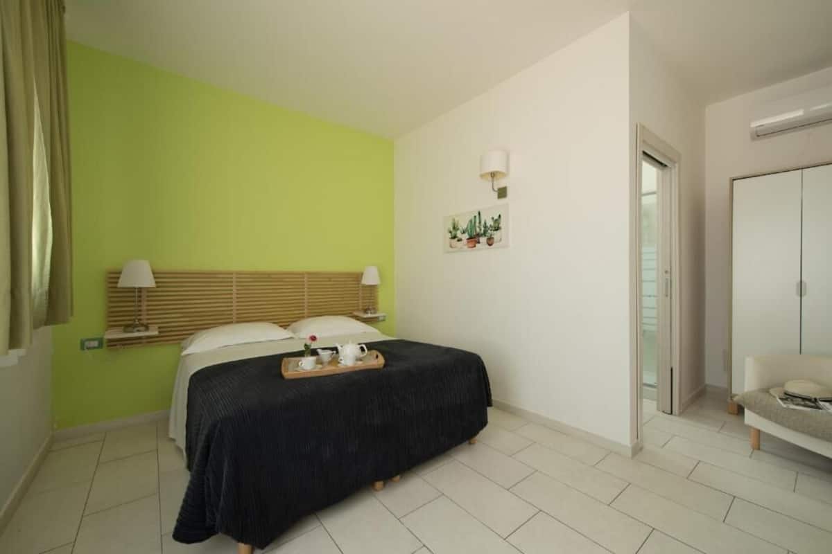 Quarto com cama, mesas de cabeceira, cômoda, espelho e parede verde.