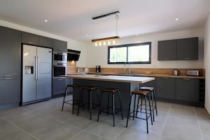 Una cocina moderna con gabinetes grises, una isla central con taburetes, horno empotrado y una ventana sobre el fregadero.