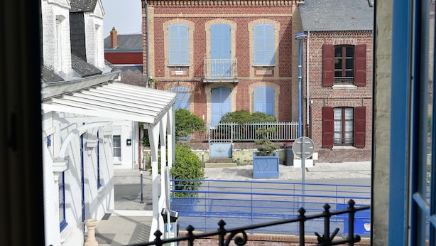 Um edifício de tijolos com persianas azuis, um portão e um edifício branco com detalhes azuis em primeiro plano.
