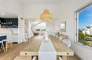 Una cocina moderna con armarios blancos, una mesa de comedor de madera y una lámpara colgante de ratán.