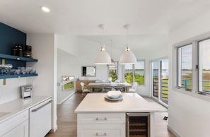 Una cocina moderna con una isla central, luces colgantes y amplios ventanales con vistas.