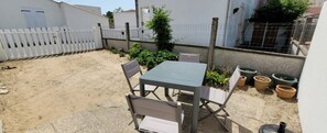 Un patio con tavolo e sedie, circondato da un recinto bianco e piante in vaso.