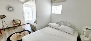 Una camera da letto con un letto, una sedia, un tavolino e uno specchio fissato alla parete.