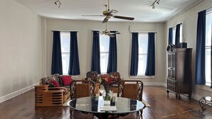 Une pièce spacieuse avec un plancher en bois, une table ronde en verre et un ventilateur de plafond.