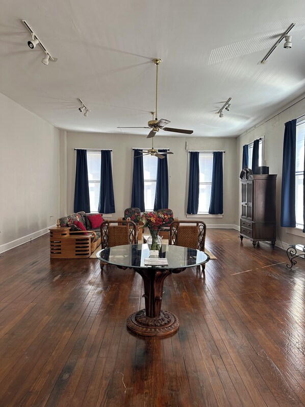 A spacious room with a wooden floor, a round glass table, and a ceiling fan.