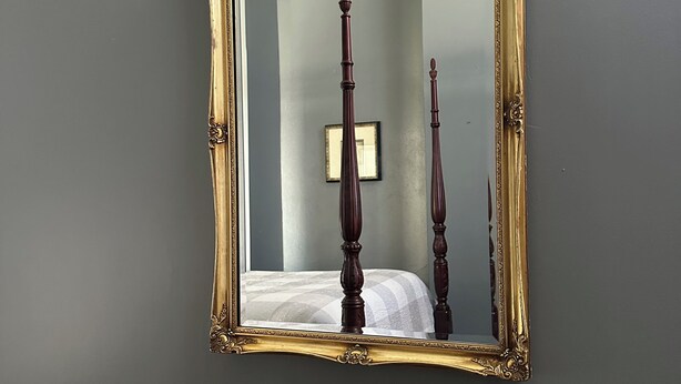 Un miroir avec un cadre doré orné, accroché à un mur gris.