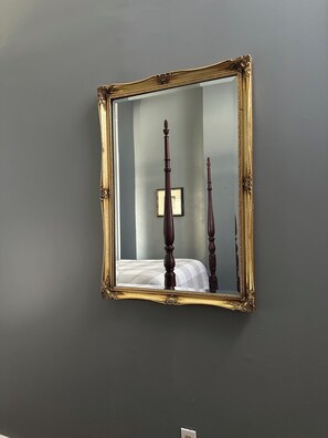 Un miroir avec un cadre doré orné, accroché à un mur gris.