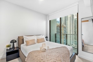 A modern hotel room with a large bed, a nightstand, a lamp, and a view of high-rise buildings. - Cozy 1BR+Den | Free Parking  | Rooftop Pool (Miami)