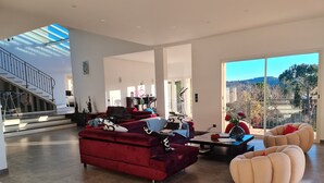 Een ruime woonruimte met een rode bank, een beige relaxstoel en een salontafel. Achtergrond toont een trap die naar een verdieping leidt.