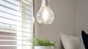 A white bedside table with a potted plant, a lamp, and a bed with white bedding.