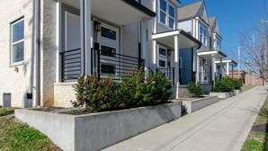 A row of townhouses with a uniform architectural style, featuring a central porch, a brick facade, and a well-maintained lawn.