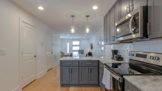 A modern kitchen with grey cabinets, a central island, stainless steel appliances, and pendant lighting.