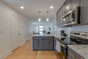 Une cuisine moderne avec des meubles gris, un îlot central, des appareils en acier inoxydable et des luminaires suspendus.