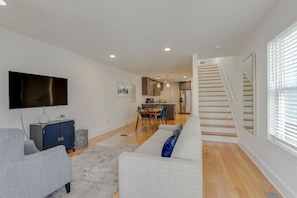 A modern living room with a sofa, TV, and a staircase leading to a kitchen area.