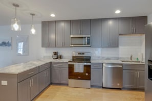 A modern kitchen with grey cabinets, stainless steel appliances, and a marble countertop.
