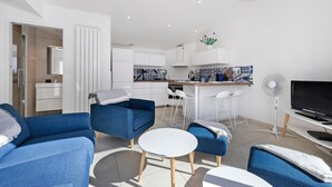Un soggiorno moderno con divani blu, un tavolo rotondo bianco e un angolo cottura con mobili bianchi e piastrelle a parete.