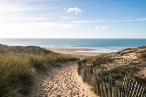 Ein Sandweg am Strand, der zum Meer führt, mit einem Holzzaun an der Seite.