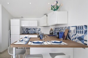 A modern kitchen with white cabinets, a wooden dining table set for two, and a backsplash with geometric patterns. - The Brisans Apartment 50m from the Beach (La Tranche-sur-Mer)