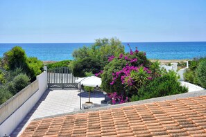 Eine Terrasse mit Meerblick, ein weißer Zaun und ein Garten mit rosa Blumen.