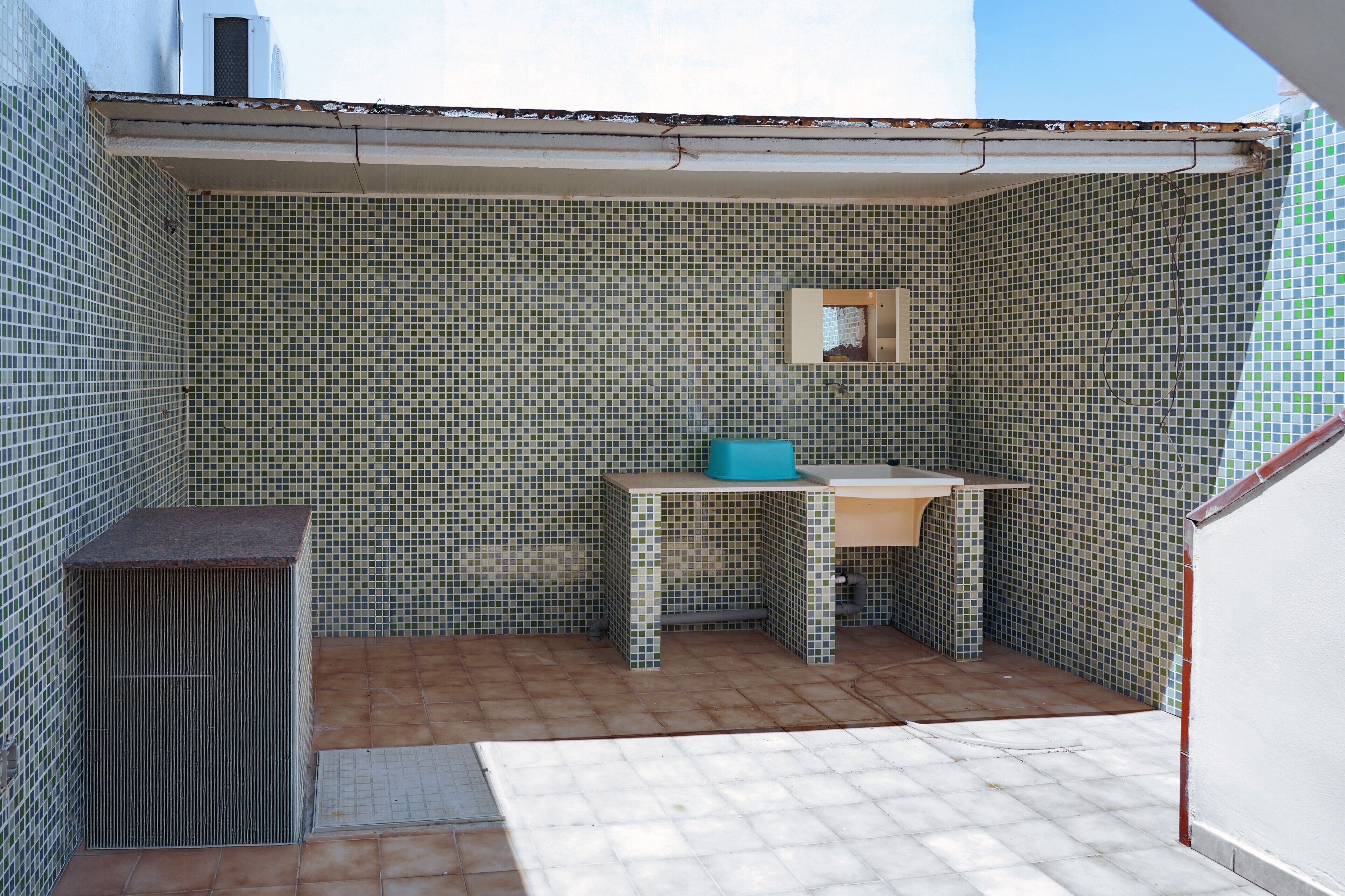 Um banheiro pequeno com parede revestida de azulejos, pia e espelho.