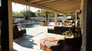 A covered patio with outdoor furniture, a pool, and a barbecue area.