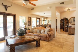 A spacious living room with a large sofa, a wooden coffee table, and a ceiling fan. - The Bradford - Southwest Luxury w/ Pool + Mountain Views in Sunny Fountain Hills (Fountain Hills)